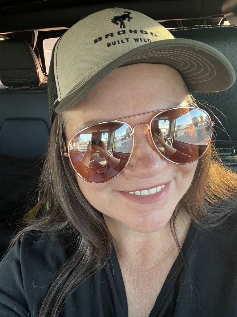 Headshot of the author, Candice Lochmanetz. Candice is sitting in a vehcicle in aviator sunglasses and a ballcap